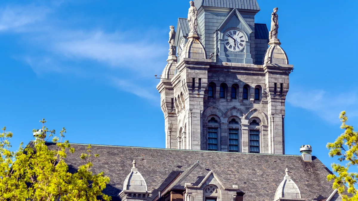A stone city hall with a clock tower stands on a cobbled main street.