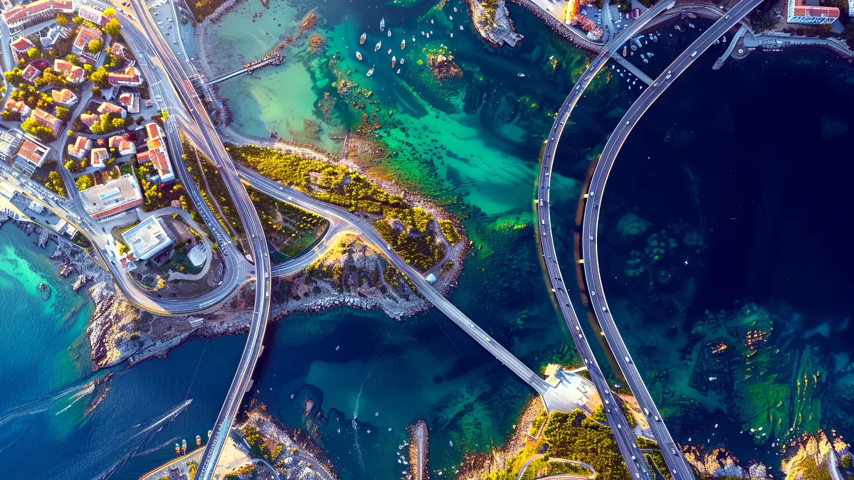 An aerial view shows a coastal city grid meeting a breakwater and open sea.